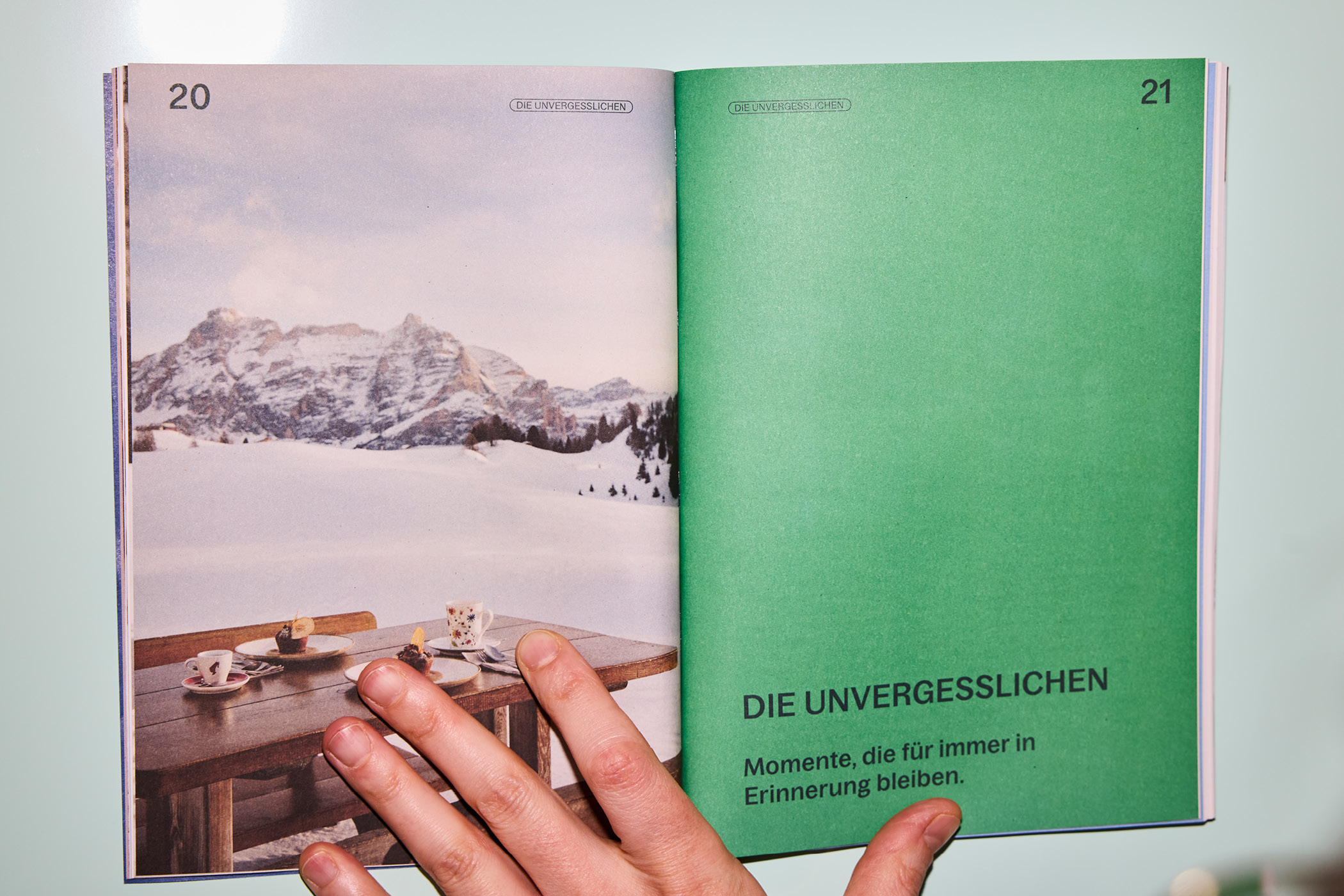 Geöffnete Broschüre mit verschneiter Berglandschaft und gedecktem Holztisch.