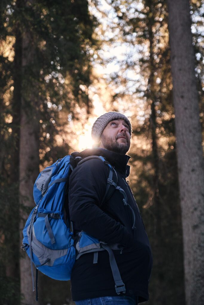 Mann mit Mütze und Rucksack im Wald, Sonnenlicht hinter ihm
