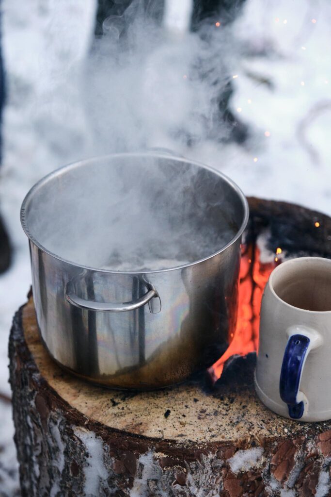 Kochtopf auf Baumstumpf über Lagerfeuer im Schnee