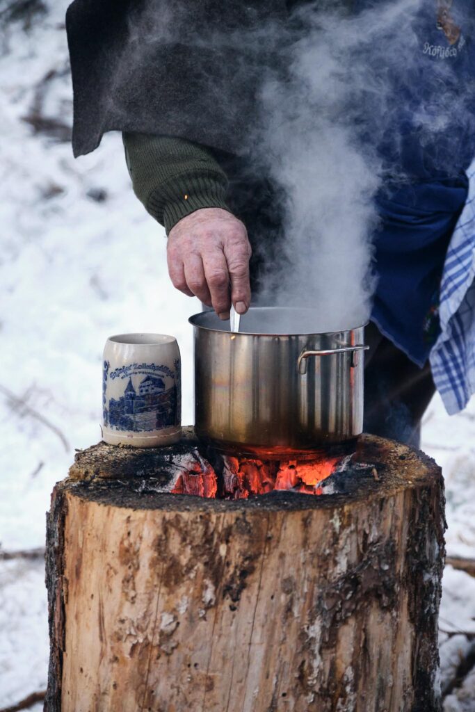 Hand rührt in dampfendem Topf auf brennendem Holzscheit