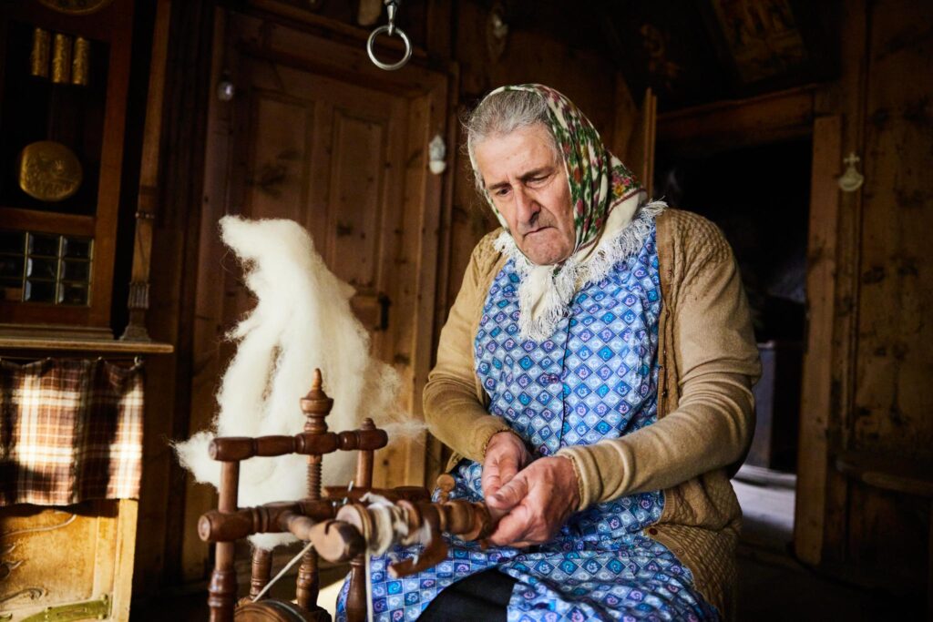 Ältere Frau spinnt Wolle an einem traditionellen Spinnrad.