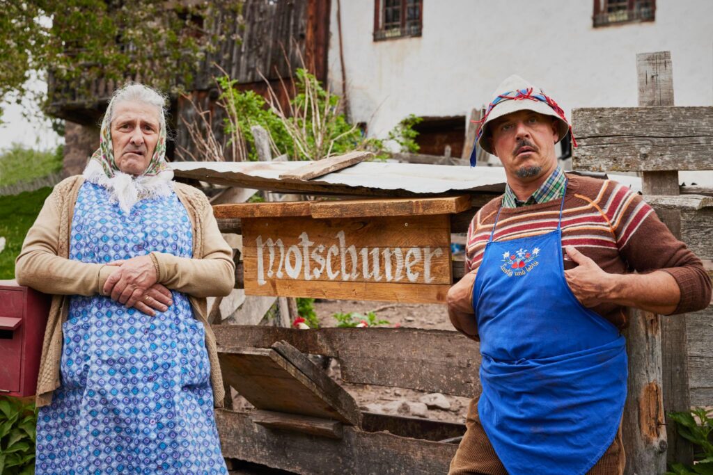 Zwei Personen vor einem Schild mit der Aufschrift 'Motschuner'.