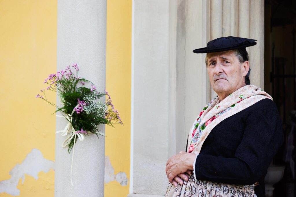 Mann in traditioneller Kleidung neben Säule mit Blumenstrauß