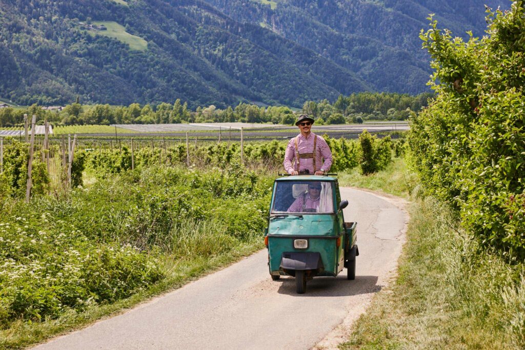 Zwei Männer in traditioneller Kleidung auf kleinem Fahrzeug, Berglandschaft im Hintergrund