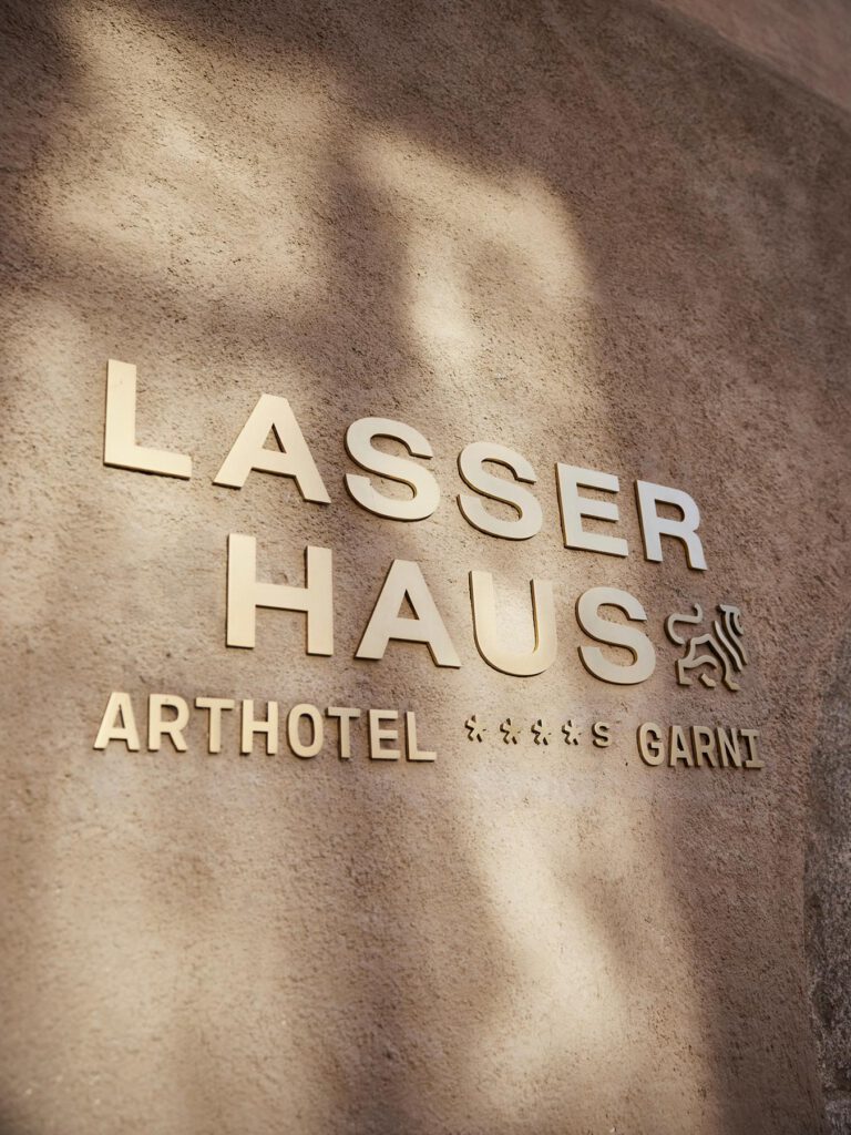 Goldene Beschriftung 'Lasser Haus Arthotel Garni' auf rustikaler Wand