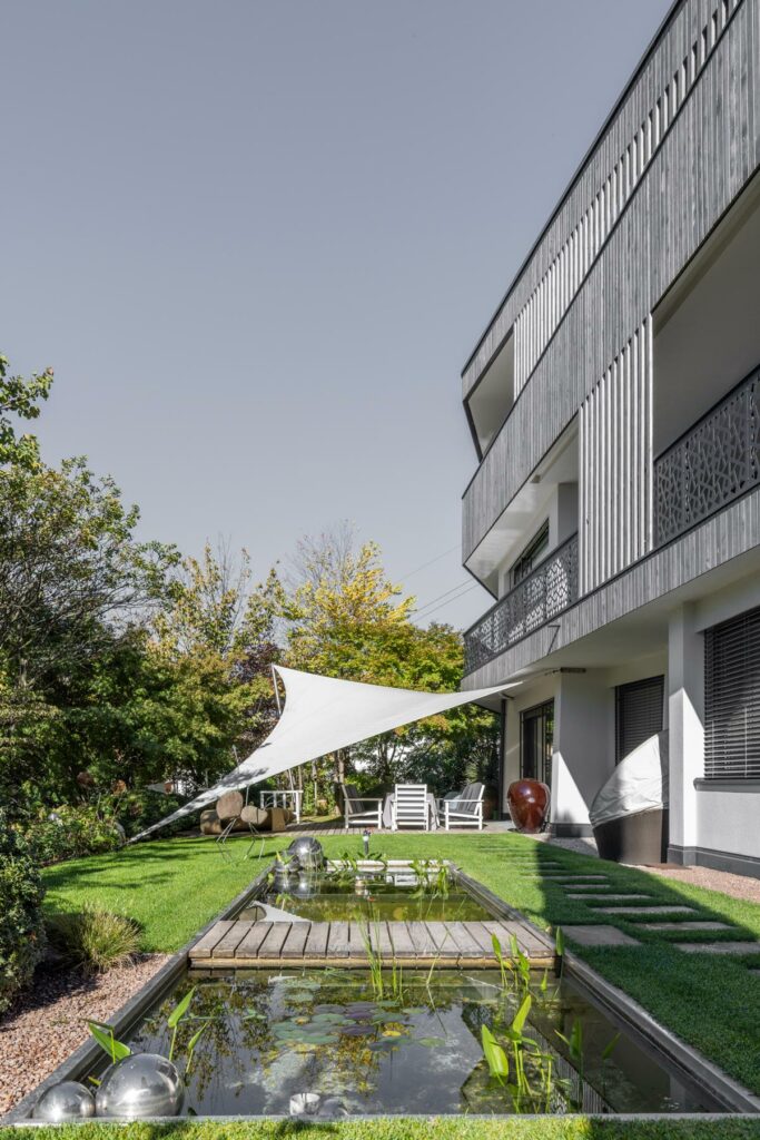 Moderner Garten mit Teich und Sonnensegel an Gebäude