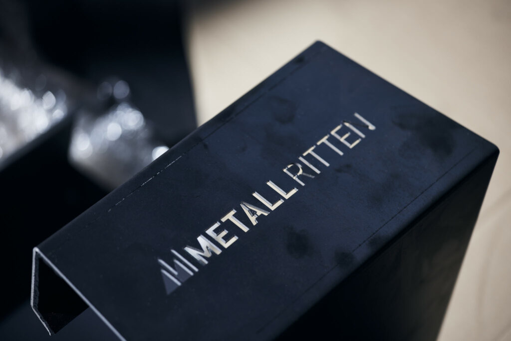 Schwarzes Metallteil mit ausgeschnittenem Schriftzug Metall Ritten.
