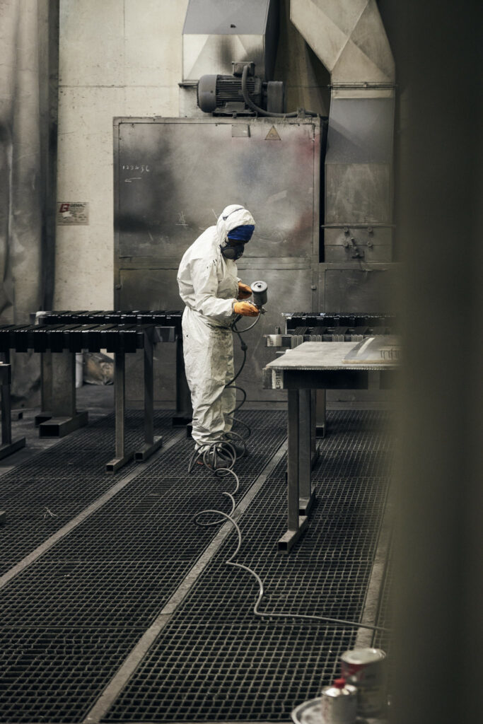 Arbeiter in Schutzanzug sprüht Metallteile in Fabrikhalle