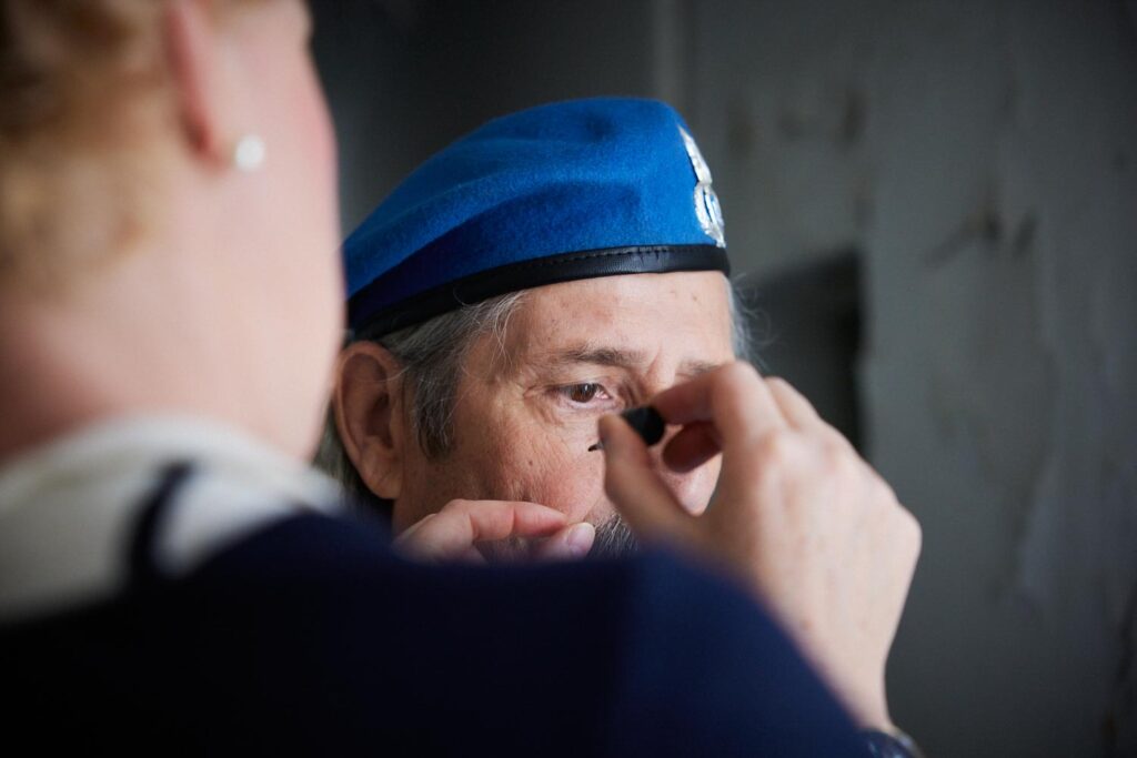 Person im blauen Barett wird geschminkt