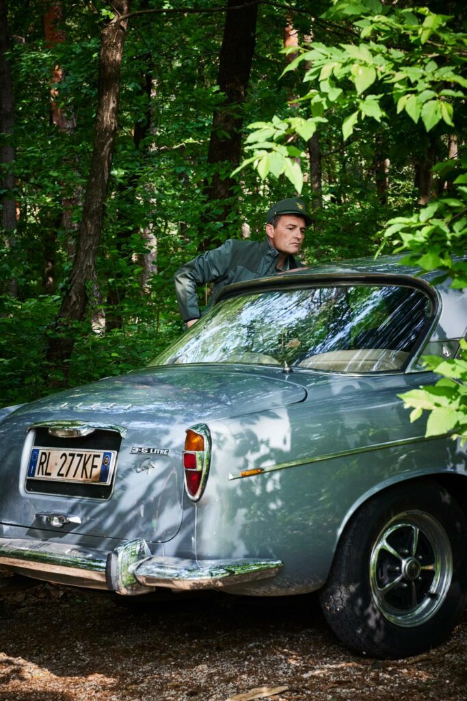 Mann in Uniform lehnt an klassischem Auto im Wald