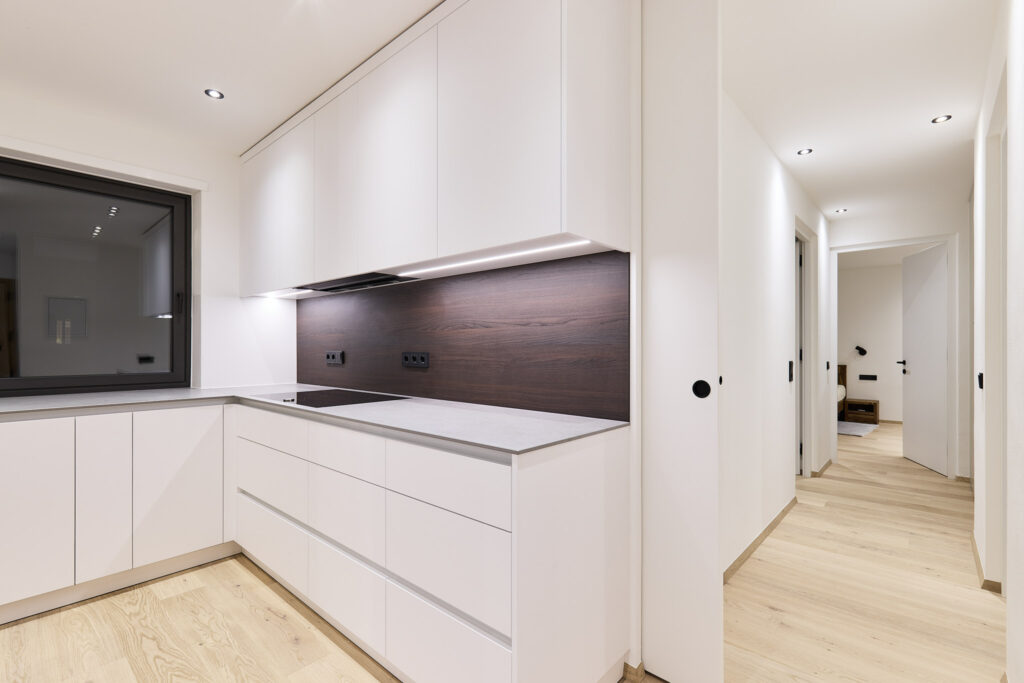 Moderne weiße Küche mit dunkler Rückwand und hellem Holzboden