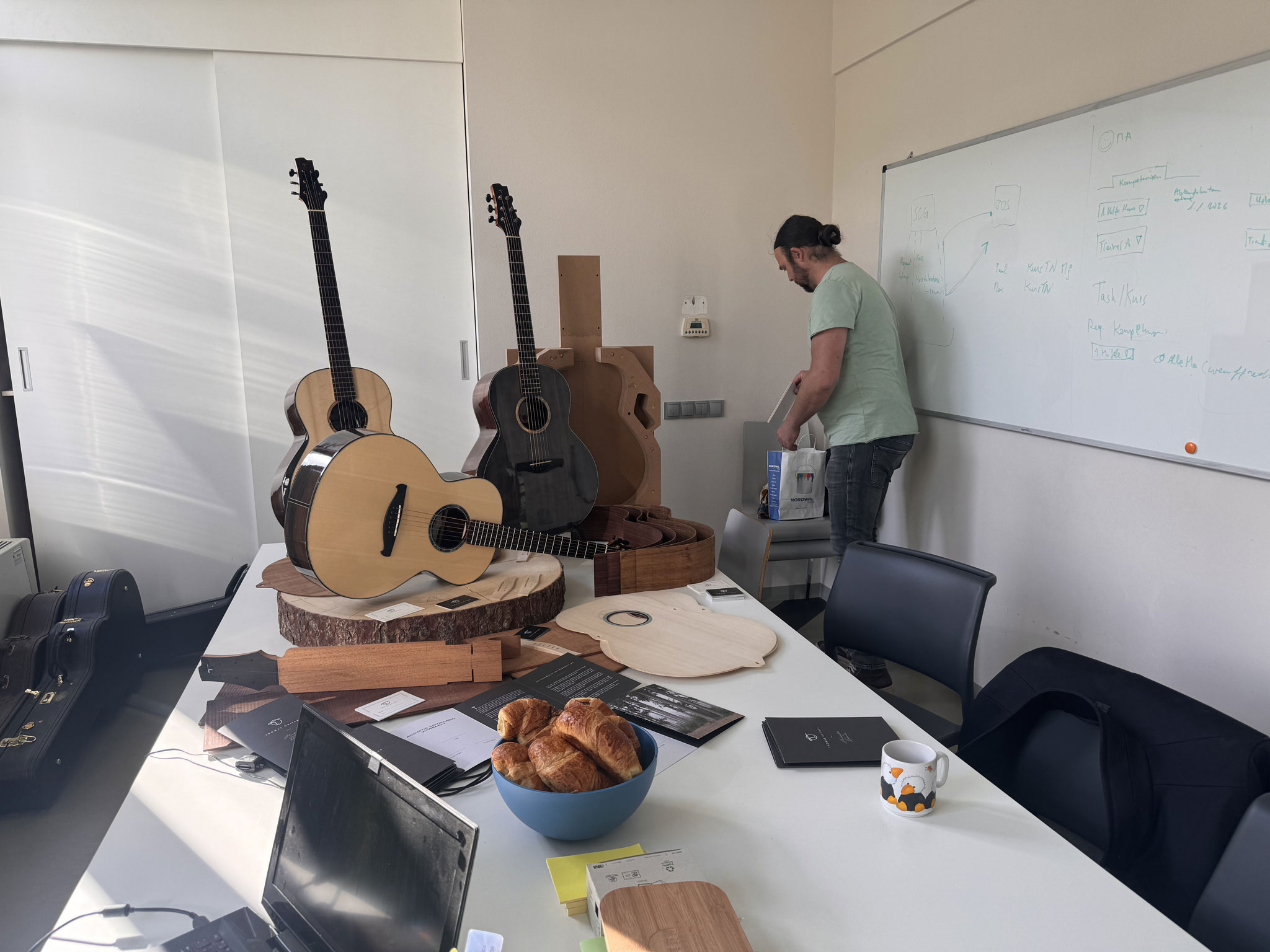 Mann richtet Besprechungsraum mit Gitarrenpräsentation und Whiteboard ein.