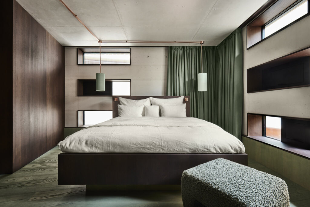 Musterzimmer mit modernem Bett, Holzwänden und grünen Vorhängen