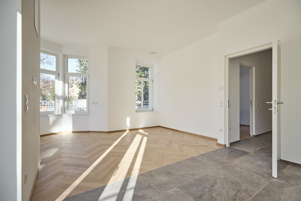 Leerer, heller Raum mit Parkettboden und großen Fenstern