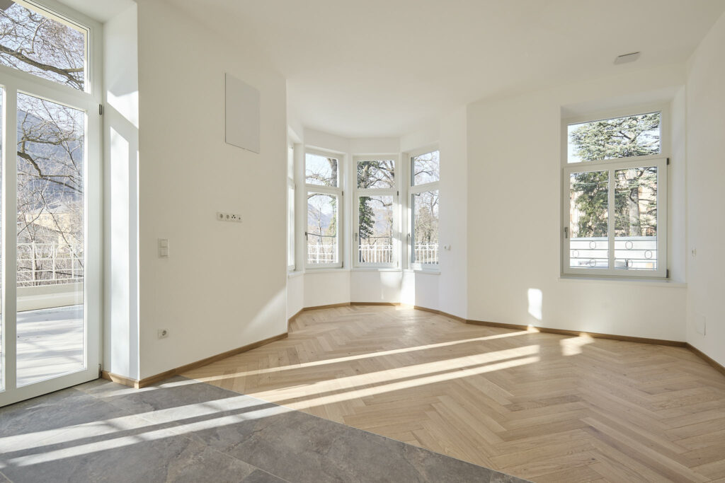 Helles, leeres Wohnzimmer mit großen Fenstern und Parkettboden