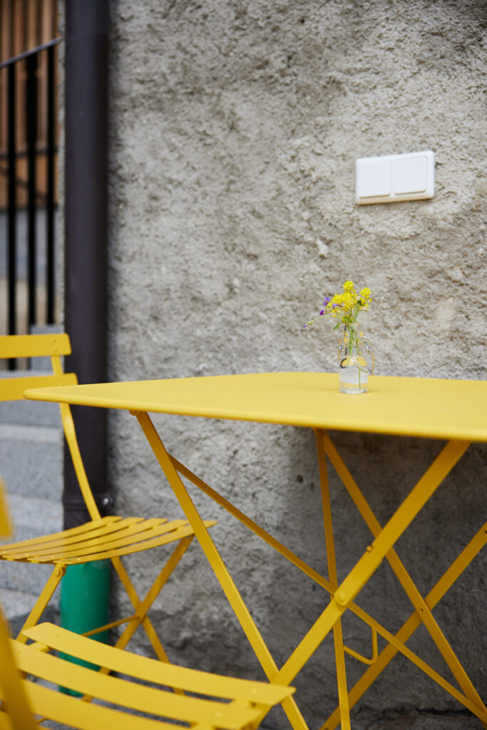 Gelber Tisch und Stuhl mit Vase vor Betonwand
