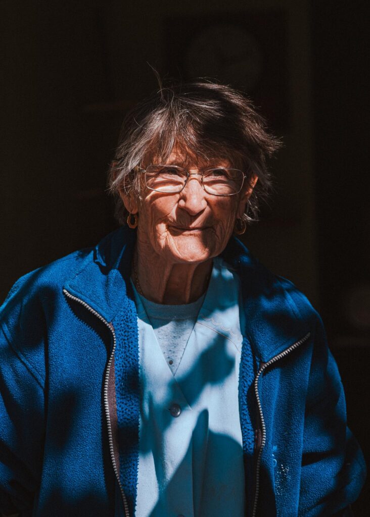 Ältere Frau in blauem Pullover, strahlend im Sonnenlicht