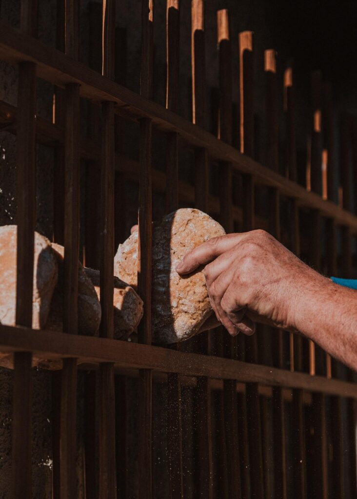 Hand legt Brot in Holzregal bei Sonnenlicht.