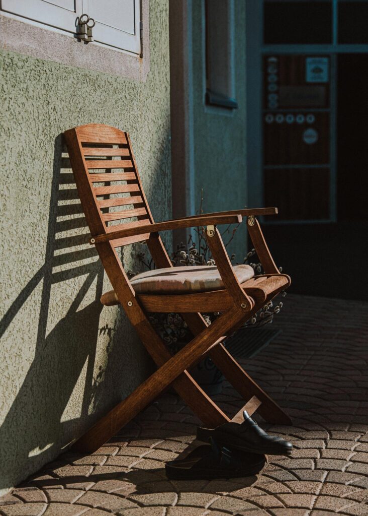 Holzstuhl an Hauswand im Sonnenlicht, Schuhe daneben auf Boden