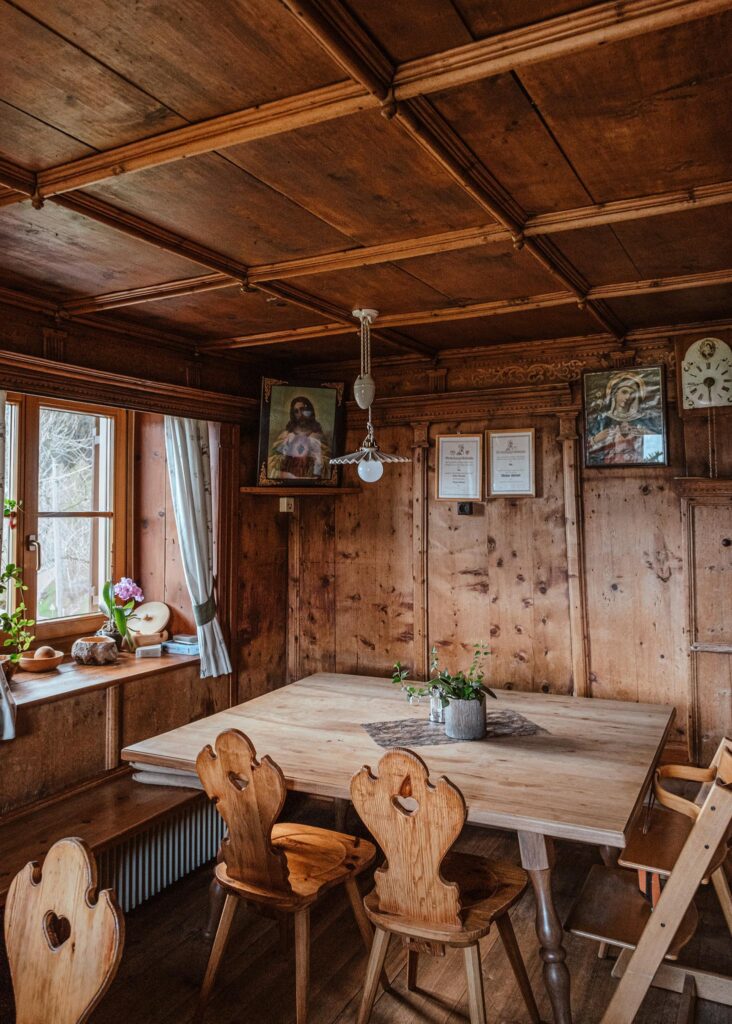 Holzgetäfelter Raum mit Tisch, Stühlen und religiösen Bildern