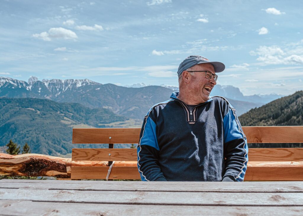 Lachender Mann auf Bank mit Bergpanorama im Hintergrund