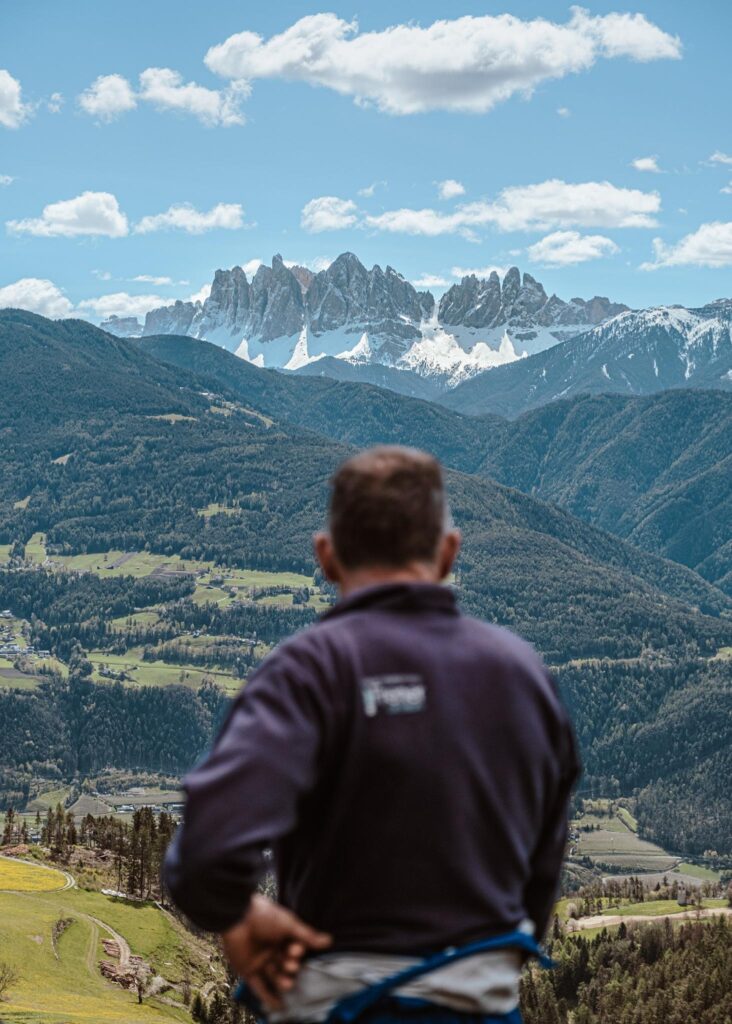 Mann blickt auf Alpenlandschaft mit schneebedeckten Bergen und blauem Himmel.