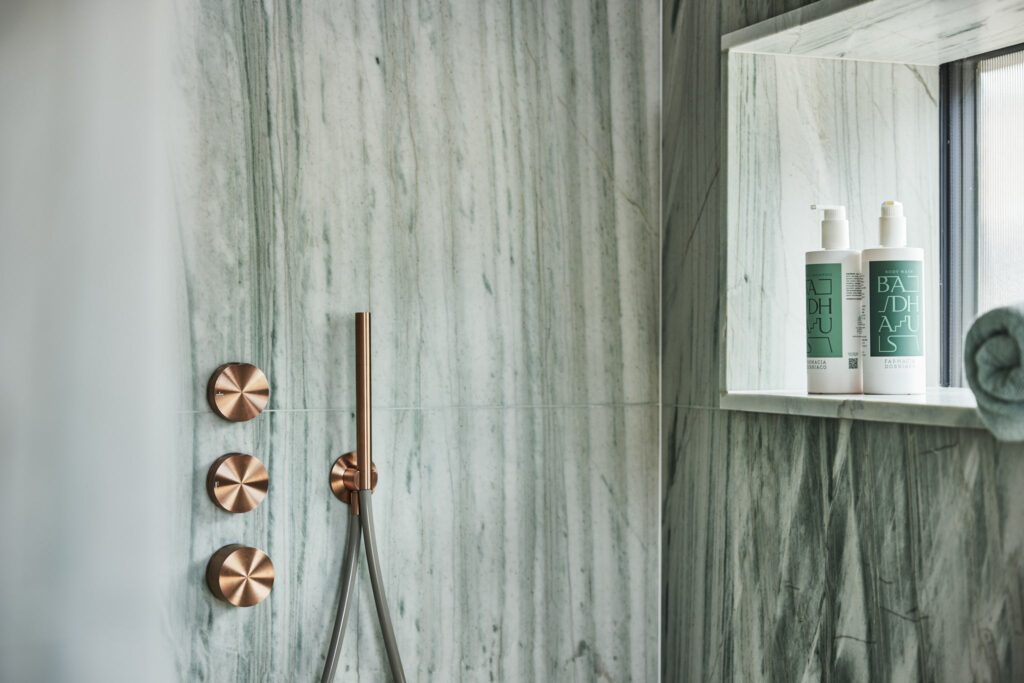 Moderne Regendusche mit Marmorwand und Pflegeprodukten im Regal