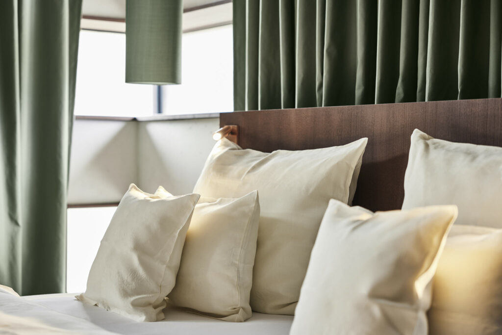 Gemütliches Bett mit Kissen, grüne Vorhänge, warmes Licht