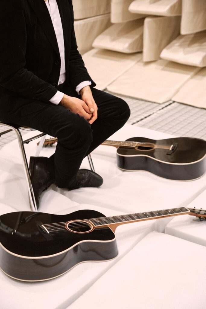 Mann in schwarzem Anzug neben zwei akustischen Gitarren
