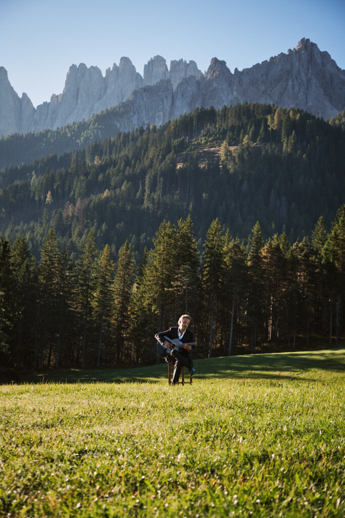 Mann mit Gitarre auf Wiese vor Bergkulisse