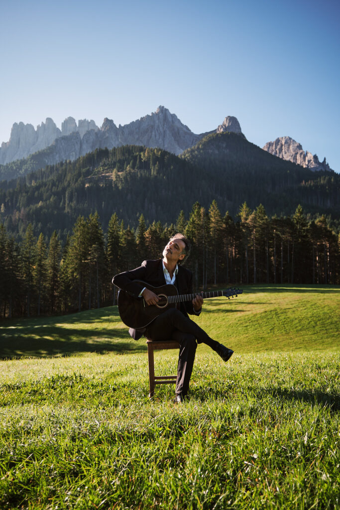Musiker mit Gitarre auf Stuhl vor Berglandschaft