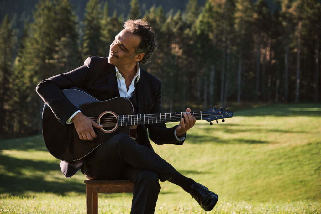 Musiker mit Akustikgitarre auf Wiese vor Waldkulisse
