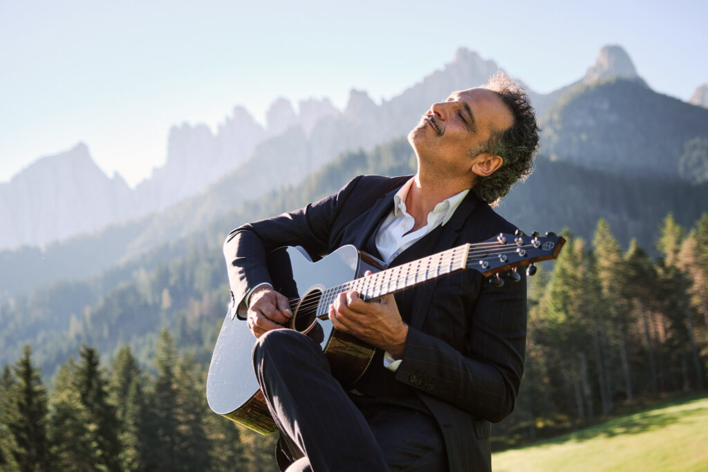 Mann im Anzug spielt Gitarre vor Bergpanorama