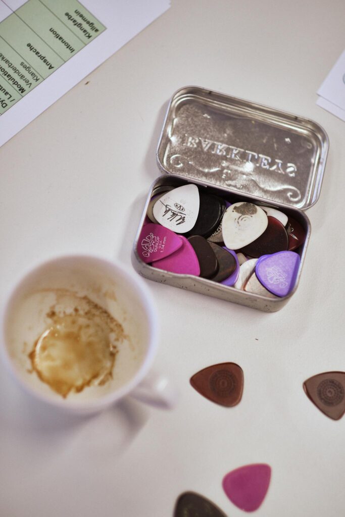 Geöffnete Blechdose mit Plektren, daneben Kaffeetasse und Notizen.
