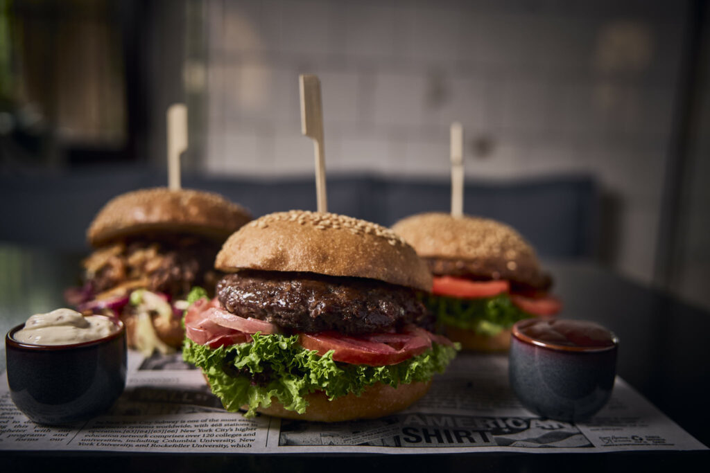 Drei Gourmet-Burger mit frischem Salat und Tomaten, Saucenbecher vorne