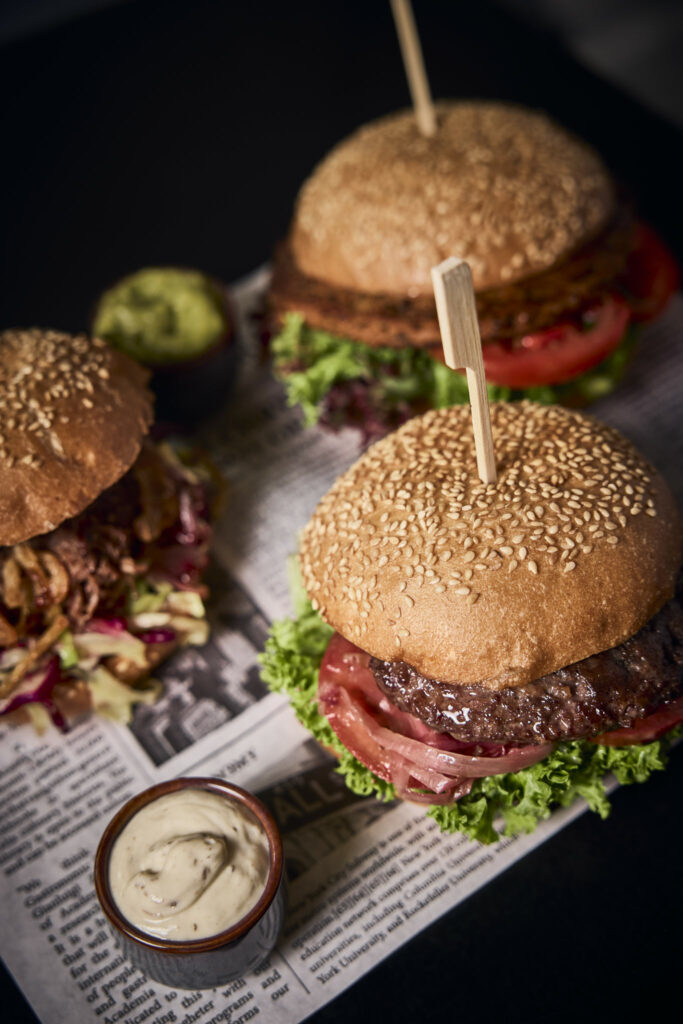 Drei Burger auf Zeitung mit Sauce und Avocado-Dipp