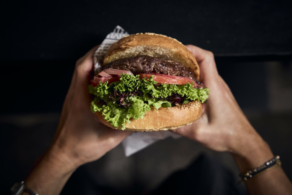 Hände halten großen Burger mit Salat und Tomaten